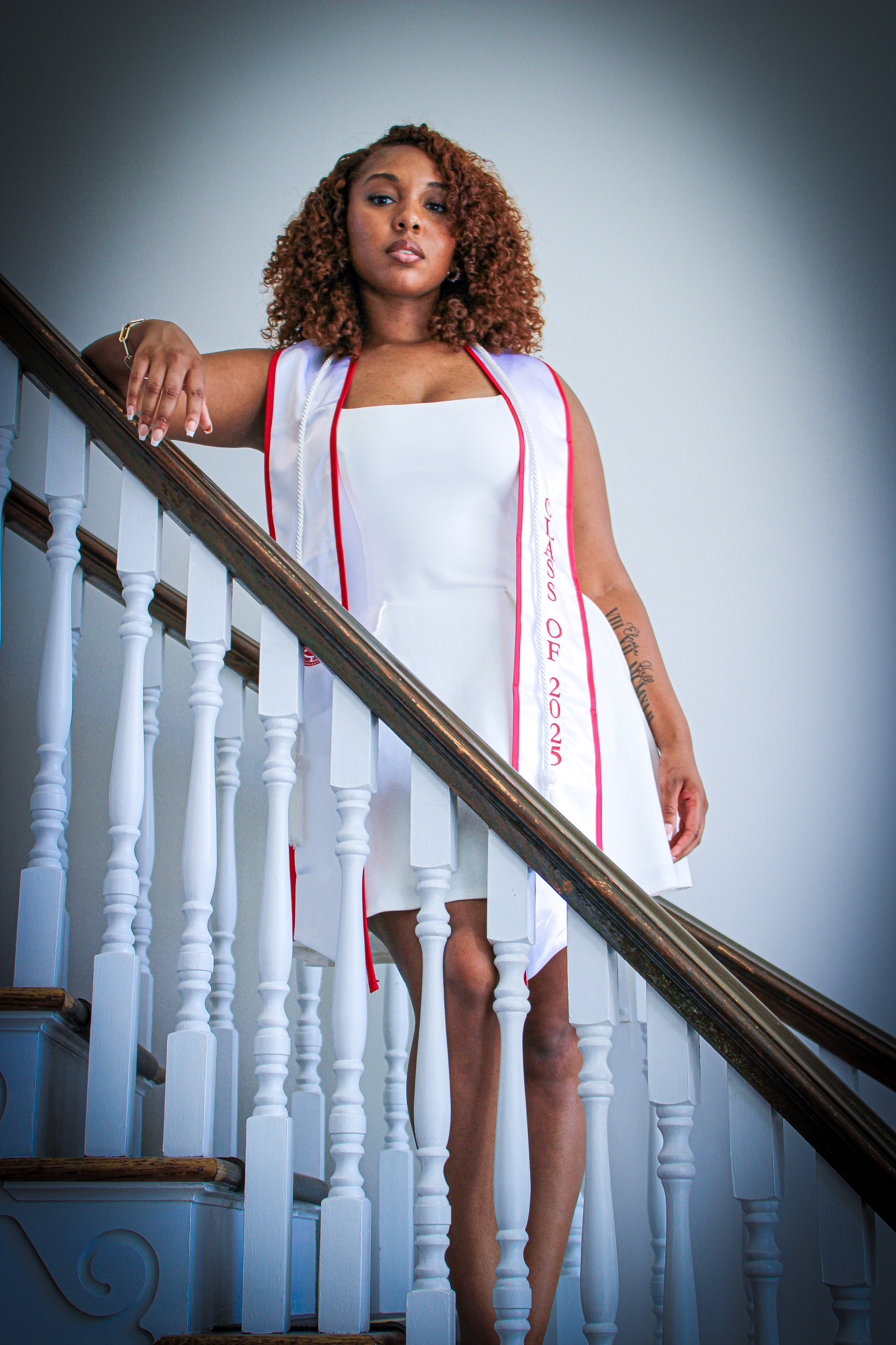 Portrait of a graduate standing on a staircase wearing a white dress and graduation stole